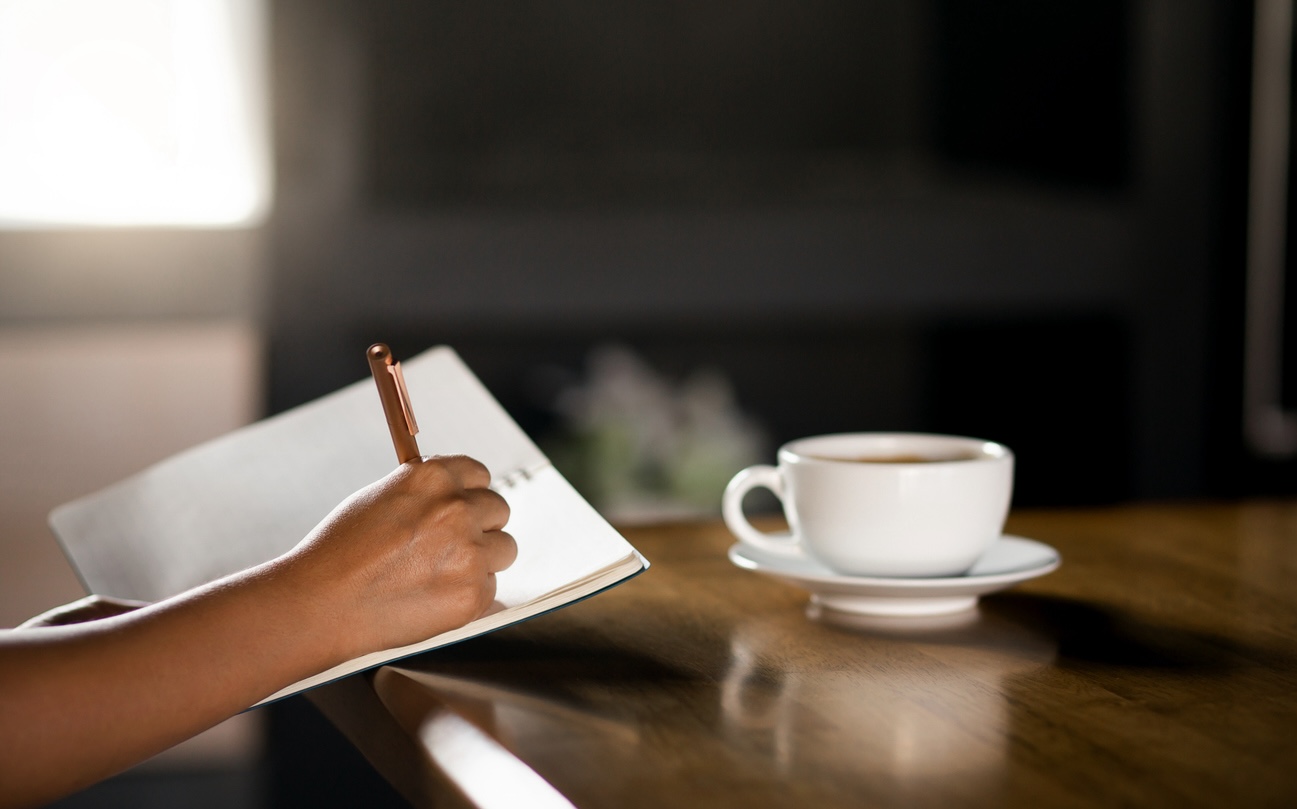 Hands writing in a journal during a morning routine, representing New Year weight loss resolutions.